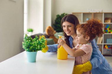 Güzel küçük kız annesinin evdeki çiçekleri sulamasına yardım ediyor, uzay mesajlarını kopyalıyor..