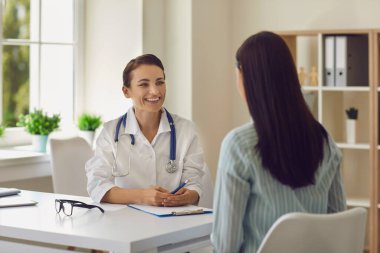 Genç, gülümseyen doktor. Klinikteki kadın hastaları dinleyen terapist.