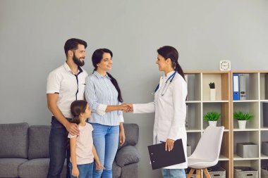 Aile doktoru el sıkışıyor. Tıp kliniğinde anne ve babaya gülümseyen bir doktor.