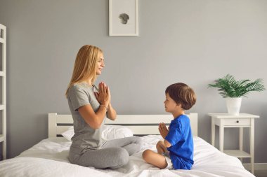 Kadın ve oğlu lotus pozisyonunda oturmuş evde meditasyon yaparken gülümsüyorlar..