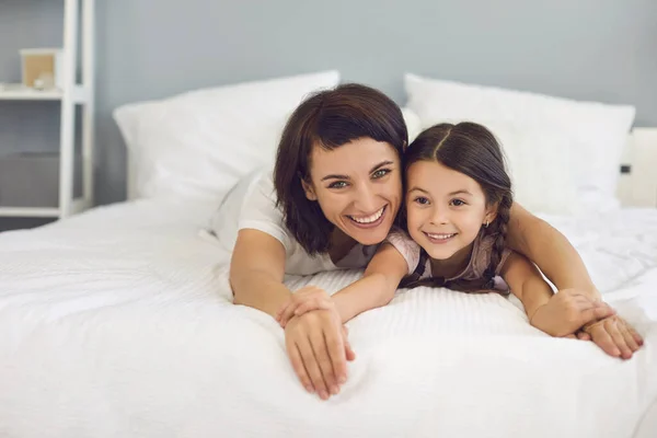 Glückliche Mutter und Tochter liegen zusammen auf dem Bett und schauen in die Kamera — Stockfoto