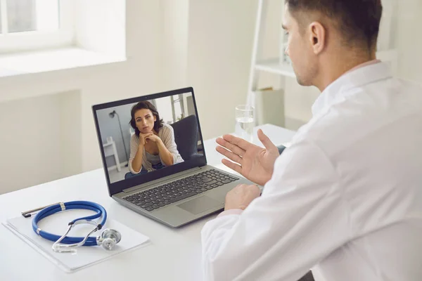 Doktor udziela konsultacji online ze swoim biurem medycznym. Męski lekarz używa laptopa i słucha pacjenta.. — Zdjęcie stockowe