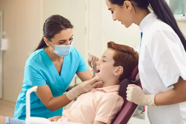 Dentysta i asystent sprawdzają zęby chłopca w klinice dentystycznej. — Zdjęcie stockowe