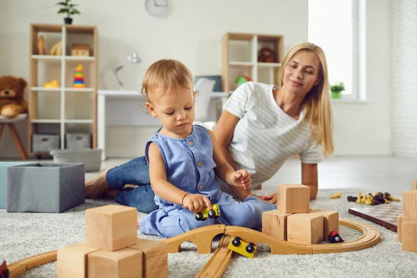Niñera joven y niño pequeño jugando con bloques de madera en la acogedora habitación del vivero —  Fotos de Stock