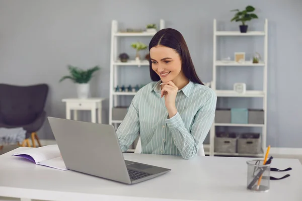 Donna sorridente che guarda il computer portatile e impara nuove informazioni durante la lezione online — Foto Stock