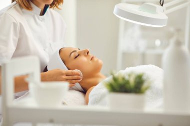 Güzellik salonunda kozmetik uzmanı kadınların yüzünü pamukla temizliyor.