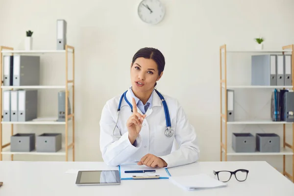 Doctor en línea. Médico femenino hispano mirando la cámara dice diagnosticar mientras está sentado en una mesa en una clínica —  Fotos de Stock