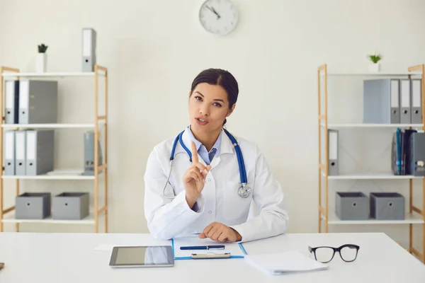 Dokter online. Spaanse vrouwelijke arts die naar de camera kijkt zegt diagnose tijdens het zitten aan een tafel in een kliniek kantoor — Stockfoto