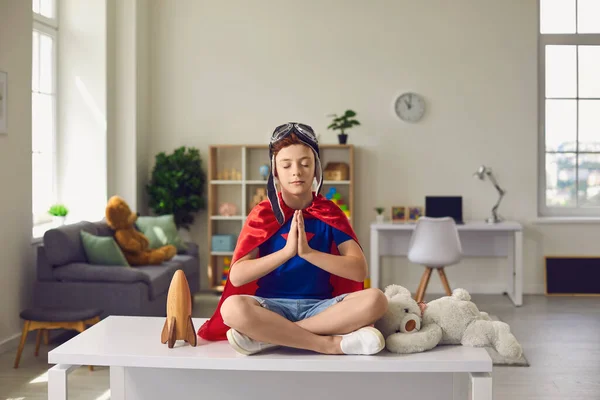 Gyerek fiú piros szuperhős köpeny és pilóta sisak meditál óvodában. — Stock Fotó