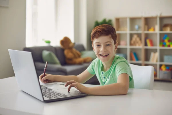 Colegial sentado en un escritorio con un ordenador portátil, escribe lecciones de la escuela durante la tarea. — Foto de Stock