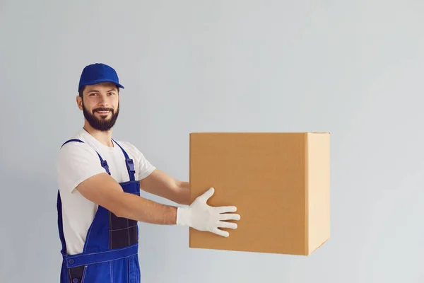 Concetto di consegna. Uomo di consegna felice con una scatola di cartone di merci su uno sfondo grigio. — Foto Stock