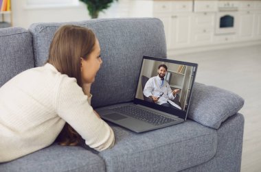 Genç bir kadın evdeki kanepede yatar ve internetten bir bilgisayarla doktora video görüşmesi yapar. Bir hastayla görüntülü görüşme.