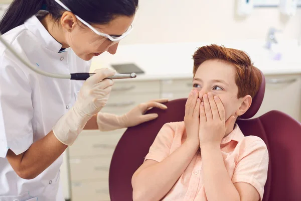 Clínica dental. Niño asustado cubriendo la boca con las manos cerca del dentista —  Fotos de Stock