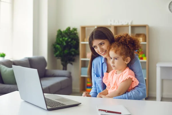 Jovem mãe e filha usando laptop para videochamada com a avó ou para assistir a vídeos educativos — Fotografia de Stock