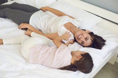 Neşeli anne ve kız evde eğleniyor, oynaşıyor ve yatakta sarılıyorlar.