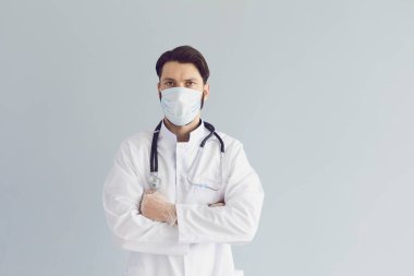 Gri arka planda çapraz kolları olan ciddi tıbbi doktor maskesi, uzay metnini kopyala. Genç doktor, çocuk doktoru ya da hemşire.