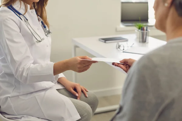 Il medico dà al paziente una prescrizione mentre è seduto sul posto di lavoro nello studio di una clinica medica. — Foto Stock