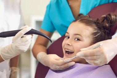 Gülümseyen kız dişlerini diş hekiminden parlak diş dolgusu ile tedavi ettiriyor.