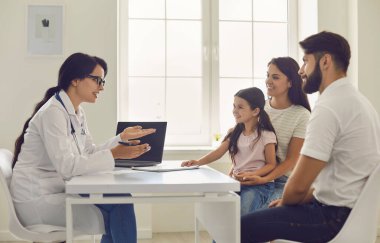 Aile doktoru. Genç kadın doktor, hastanede masada oturan küçük bir kızla ailesine danışmanlık yapıyor.