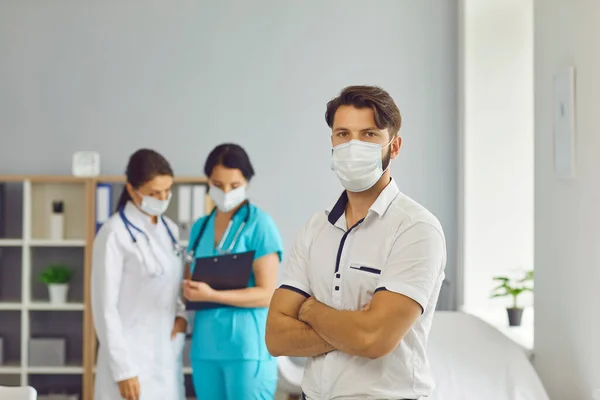 Male patient in a medical mask on the background of two female doctors. — Stock Photo, Image