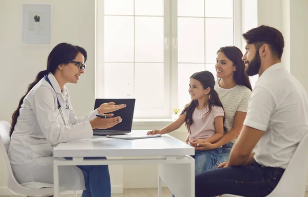 Doctor de familia. Mujer joven médico consulta a los padres con una niña sentada en la mesa en el hospital —  Fotos de Stock