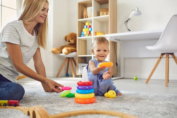 Feliz joven madre y su pequeño hijo juntos montan una colorida pirámide sentada en el suelo. —  Fotos de Stock