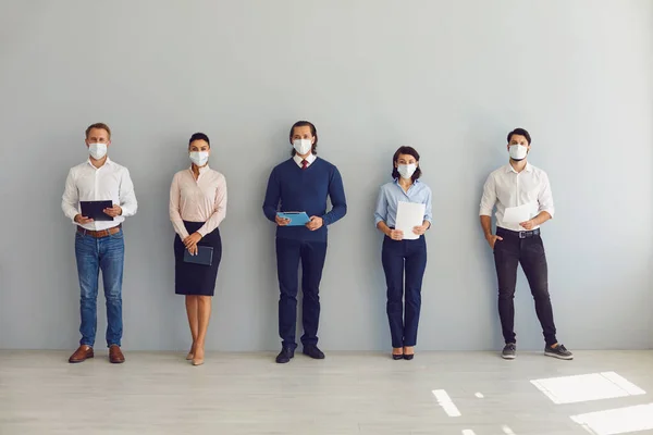 Ищущие работу в масках для лица ждут собеседования стоя в коридоре, сохраняя безопасное расстояние — стоковое фото
