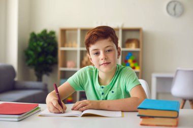 Ciddi bir öğrenci öğretmeniyle çevrimiçi konferans sırasında kameraya bakıyor ve notlar alıyor. Çocuk evden ders çalışıyor