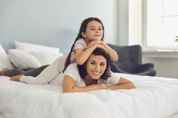 Kleines Mädchen spielt morgens im Schlafzimmer mit ihrer Mutter und legt sich auf sie. — Stockfoto