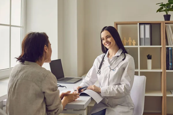 Lächelnder Arzt hört sich Beschwerden einer Patientin während des Besuchs in der Klinik an — Stockfoto