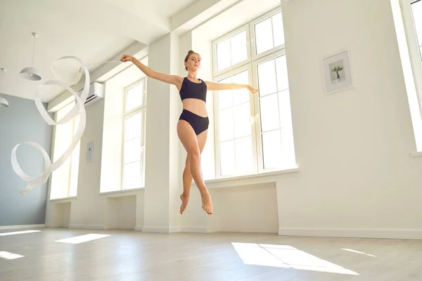 Girl jumping and practicing rhythmic gymnastics with ribbon in studio — Stock Photo, Image