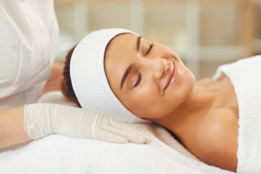 Cilt bakımı ameliyatından sonra gözleri kapalı bir şekilde spa yatağında gülümseyen genç bir kadın.