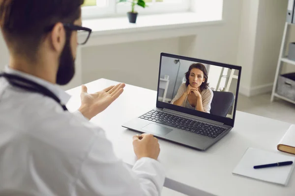 Online orvosi konzultáció. Egy férfi ül az irodájában használ egy laptopot, egy videohívást és hallgat egy beteget.. — Stock Fotó