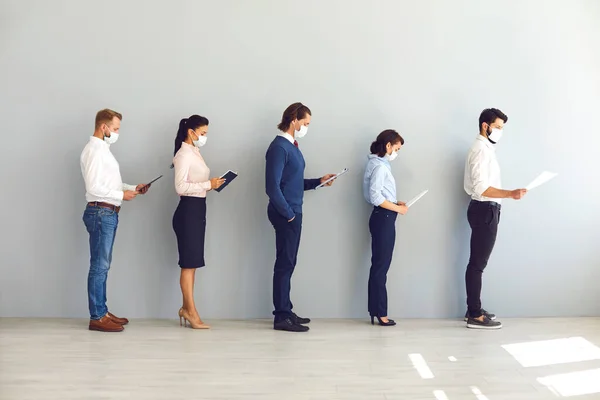 Grupo de empresários com máscaras em pé com documentos em linha e mantendo a distância no escritório — Fotografia de Stock
