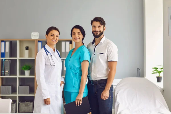 Retrato em grupo de três jovens prestadores de cuidados de saúde sorridentes no escritório da clínica moderna — Fotografia de Stock