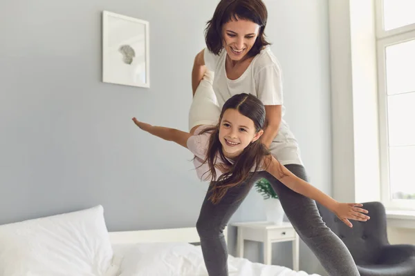 Happy mother and her daughter have fun playing together on the bed at home.