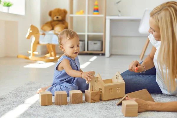 Joven niñera alegre y niño pequeño jugando con bloques de madera en la habitación acogedora —  Fotos de Stock