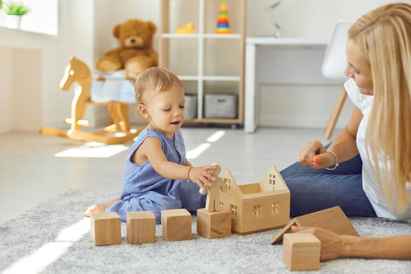 Pengasuh muda yang ceria dan anak kecil bermain dengan balok kayu di kamar yang nyaman — Stok Foto