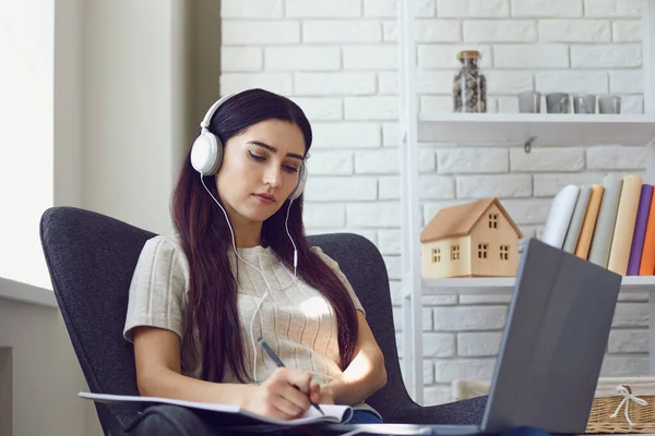 Hübsches junges Mädchen mit Kopfhörern hört Webinar, Online-Konferenz oder Geschäftstreffen zu Hause am Laptop — Stockfoto