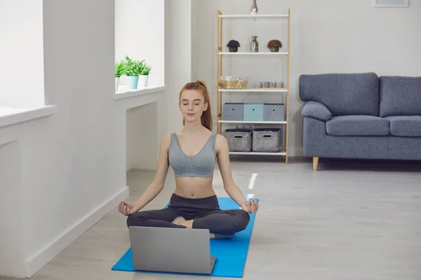 Молода дівчина сидить і медитує під час онлайн-класу йоги вдома — стокове фото