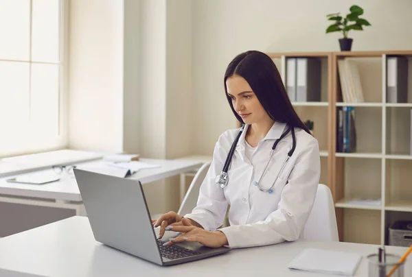 Doctora joven escribiendo en la red de navegación palabra clave portátil en la oficina del hospital moderno — Foto de Stock