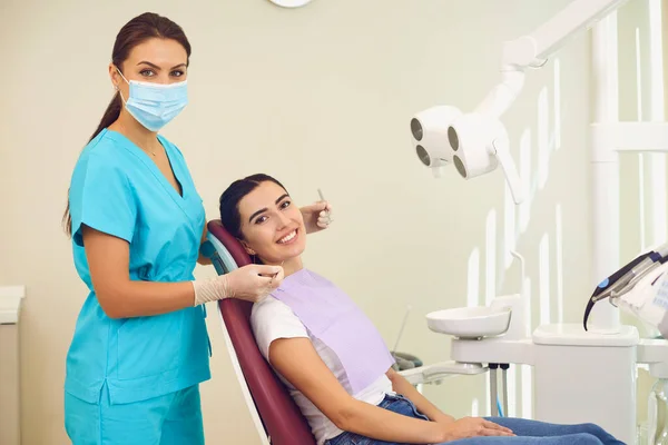 Woman doctor dentist and positive woman patient looking ar camera during tooth examination — Stock Photo, Image