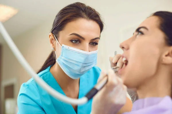 Lekarz dentysta w masce medycznej podejmowania profesjonalne leczenie zębów dla kobiety pacjenta w klinice stomatologicznej — Zdjęcie stockowe
