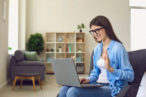 Junge Frau mit Brille macht Videoanruf am Laptop und winkt Verwandten oder Kollegen zu — Stockfoto