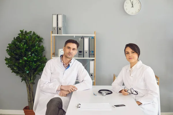 Kobieta i mężczyzna lekarze siedzący i patrzący przed kamerą w klinice medycznej — Zdjęcie stockowe