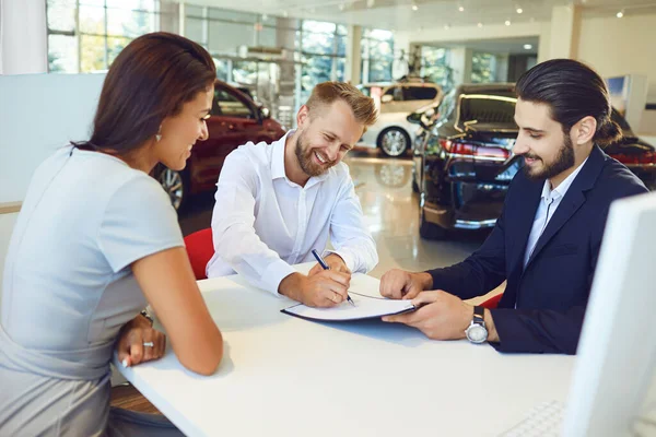 Un uomo e una donna sorridenti comprano un'auto in uno showroom di auto. — Foto Stock