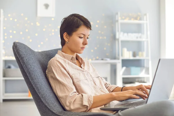 Geschäftsfrau arbeitet am persönlichen Laptop und sitzt im bequemen Sessel im gemütlichen Homeoffice — Stockfoto