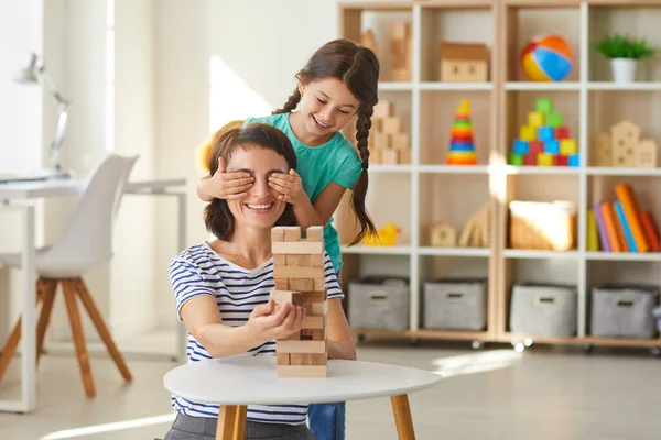 Little daughter putting hands over mommys eyes while playing with wood blocks in modern nursery — Stock Photo, Image