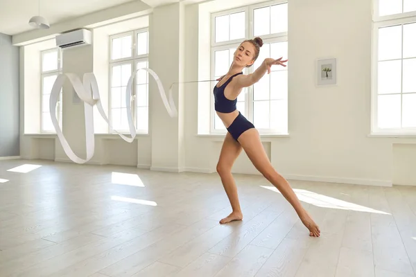 Young gymnast in black clothes with a ribbon performs an element of rhythmic gymnastics in the gym — Stock Photo, Image