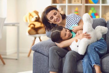 Mutlu anne ve kız kanepede dinleniyor ve evde oyuncaklarla oynuyor.